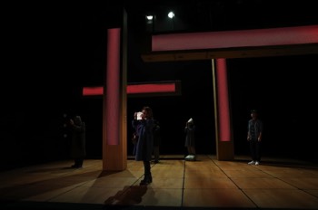  Missing People Production Image. Linda (Ishia Bennison) stands centre stage taking a selfie on her phone. Large column-like LED screens in red hang vertically and horizontally behind, to sort of look like a Japanese shrine entrance. 
