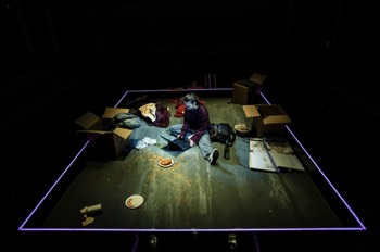 Dani (Jessica Rhodes) sits on the floor with a laptop between her legs. She's surrounded by boxes, and some left over bowls and an empty bottle of wine. The 90s style Dell laptop is plugged in to the edge of the stage, which is illuminated in a dim purple LED surround. It's dark and she's lit very dimly. The view is looking down on her on the floor, her hands rest on the keyboard.