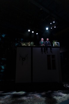 Ivy (Jenny Rainsford) and Gary (Nathan McMullen) sit on top of a building in the forest at night.