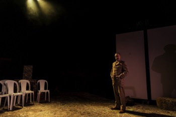 Tig (Tim Treloar) stands in the centre of a mostly empty stage in the shadows.