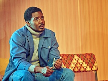 Jitney Production Image. Youngblood (Solomon Israel) sitting on a 1970s style chair.