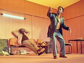 Jitney Production Image. Fielding (Tony Marshall) points beyond the camera looking slightly drunk, while Turnbo (Sule Rimi) sits reclined on a bench with a hat over his eyes.