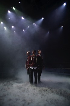 Three school boys in full school uniform stood with the backs to one another amongst thick low fog, each looking outwards.