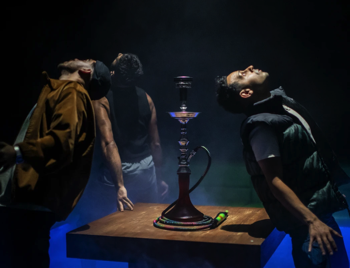 The cast leaning back towards a shisha pipe in a sunken pit surrounded by low fog.