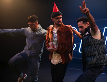 The cast celebrating with Jihad (Omar Bynon) wearing a party hat holding a birthday cake looking confused.