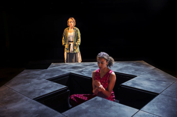 Flo (Jessica Clark) stood looking at and Bel (Ruby Crepin-Glyne) sat in the cross shaped recess in the centre of the stage.