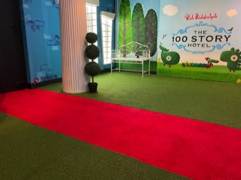 The 100 Story Hotel front entrance garden and red carpet leading to the front door between two grand columns.