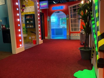 A photo of the central hallway in the 100 Story hotel. At the end is an archway into Chilly’s Sushi Bar igloo, to the left is the doorway into Zorg’s emporium with the door surrounded by blinking lights. The floor is red carpet, and a pool of fluorescent green slime is seeping out below one of the doors.