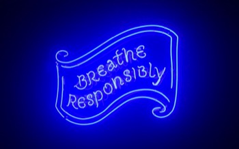 A neon sign of a scroll with Breathe Responsibily written on it.