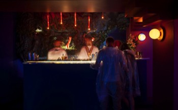 Guests standing in waterproof ponchos at the bar, the barmen blurred as they make cocktails.